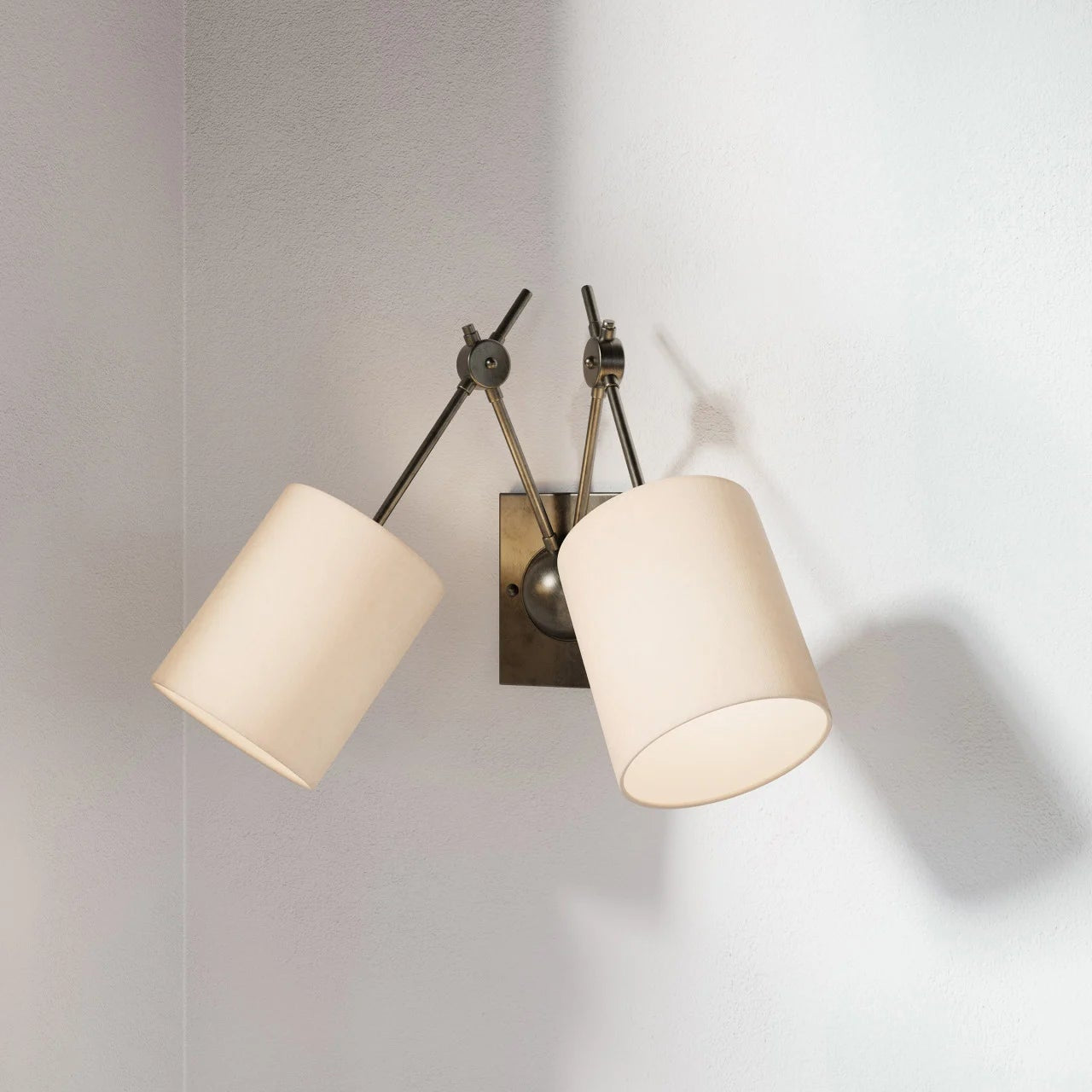 Wall-mounted lamp with two beige lampshades on a light gray wall.