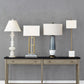 Console table with four different styled lamps against a gray wall.