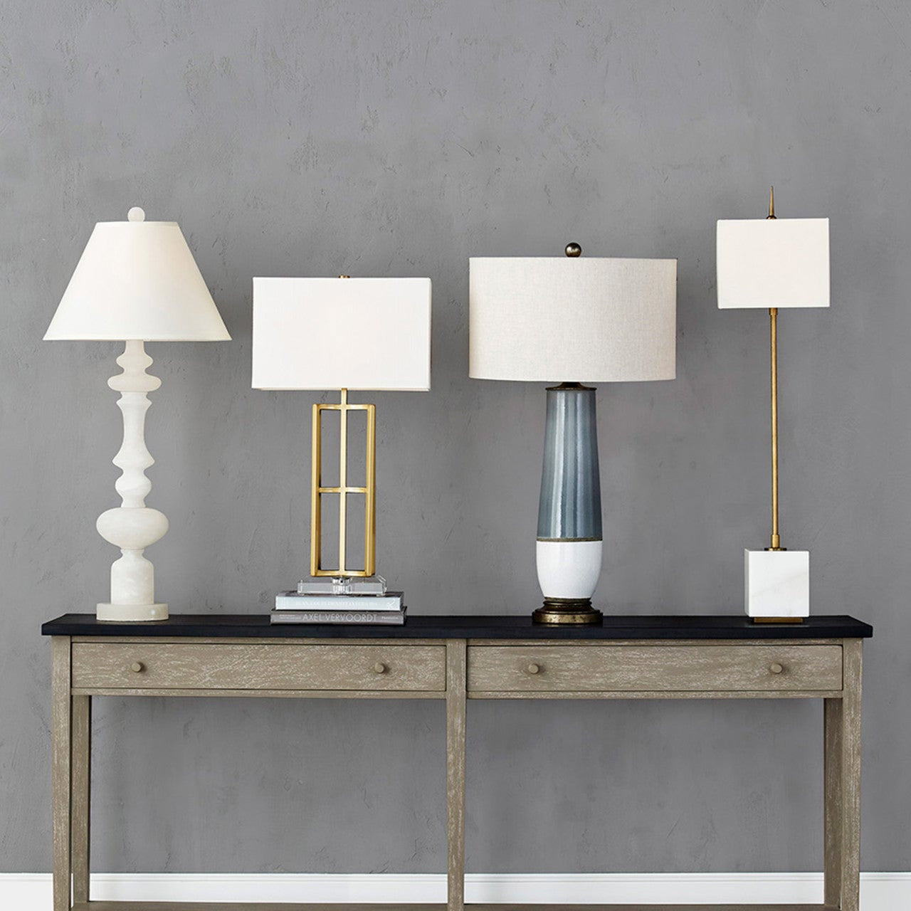 Console table with four different styled lamps against a gray wall.