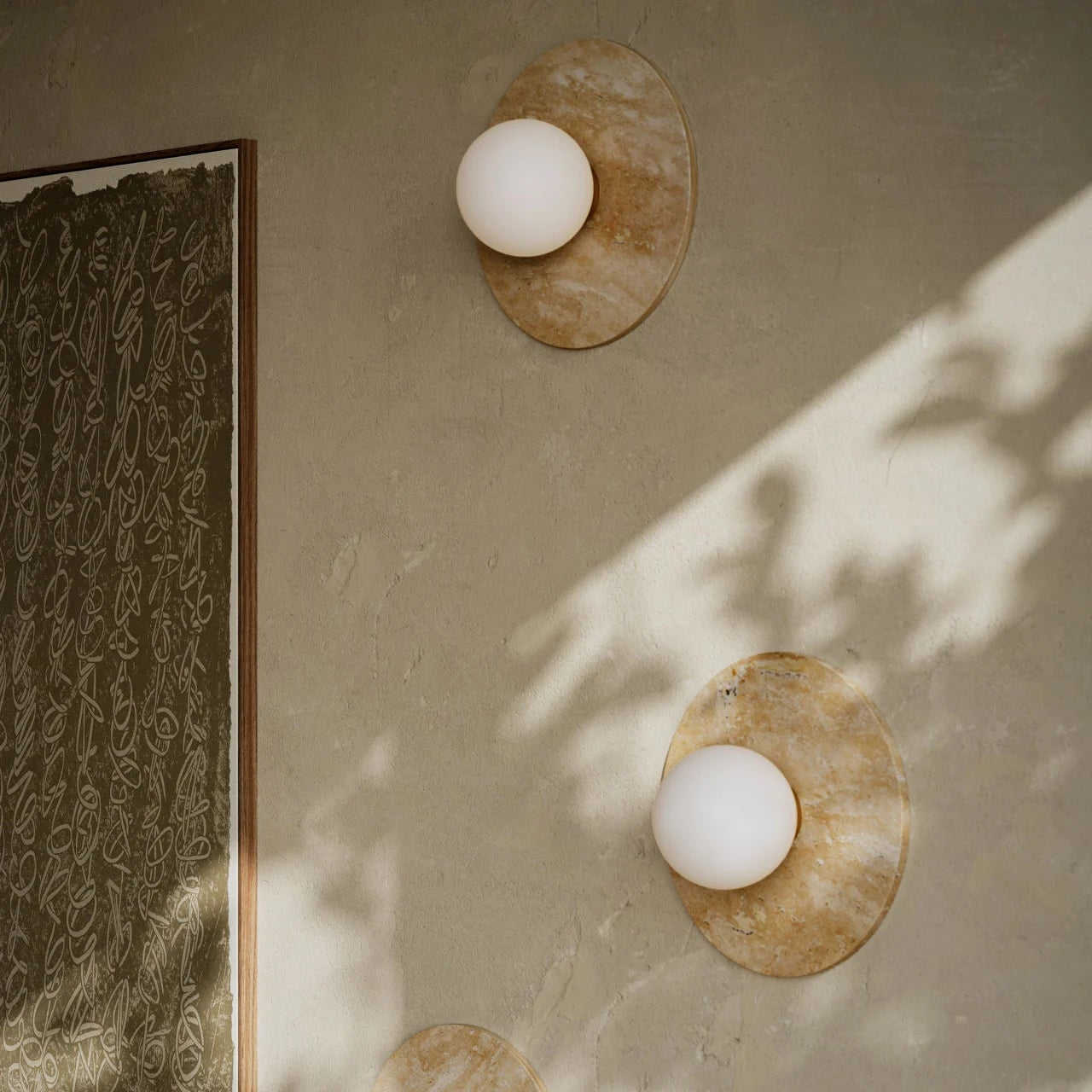 Three wall-mounted lights on a beige wall with a framed artwork to the left.