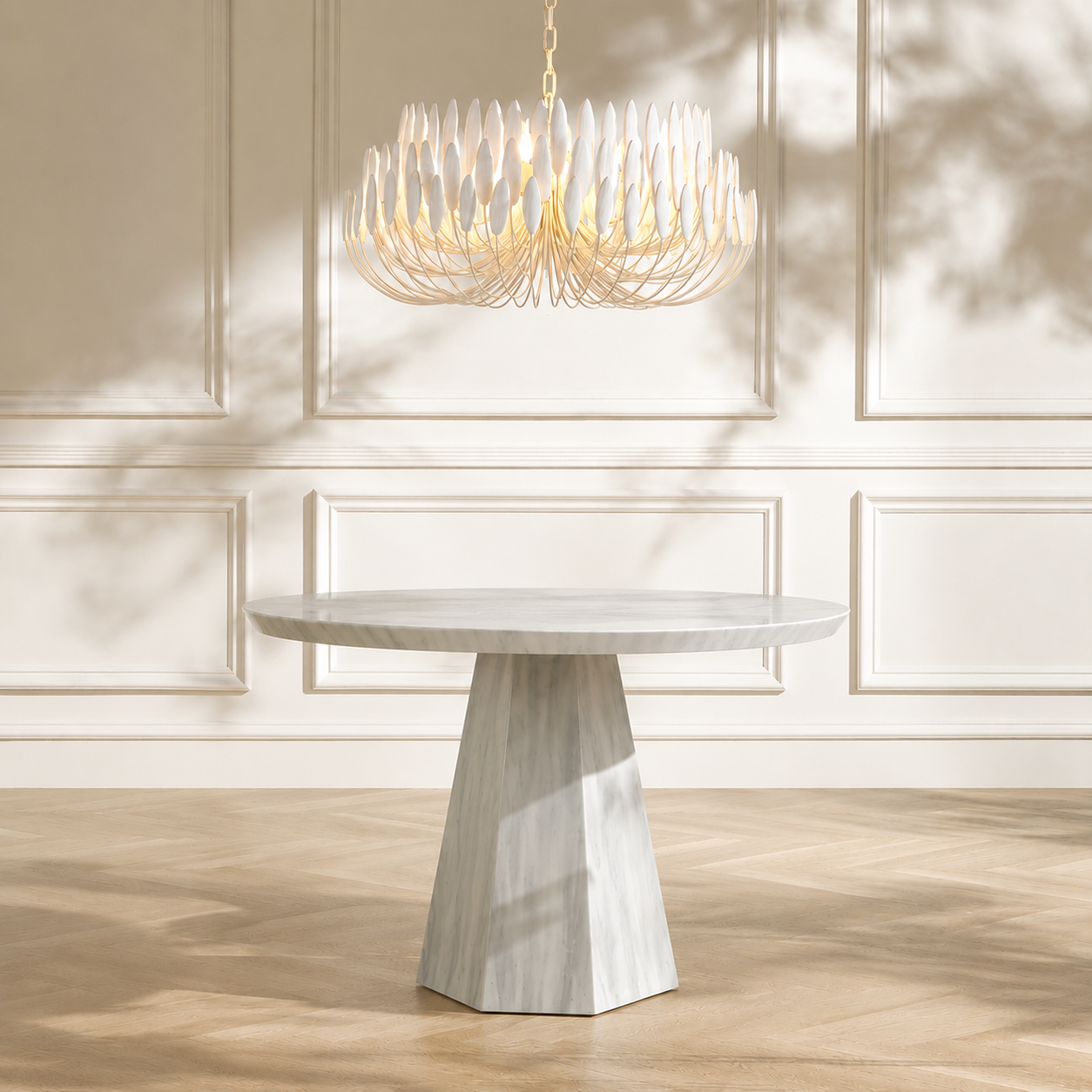A modern round dining table with a white marble top and a sculptural hexagonal pedestal base, shown in a bright room with a matching light fixture and paneled cream walls.