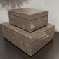 Three stacked rectangular storage boxes with a textured brown and beige animal-print pattern, displayed on a dark wooden surface against a light gray wall.