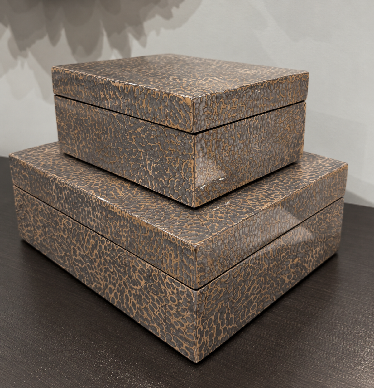 Three stacked rectangular storage boxes with a textured brown and beige animal-print pattern, displayed on a dark wooden surface against a light gray wall.