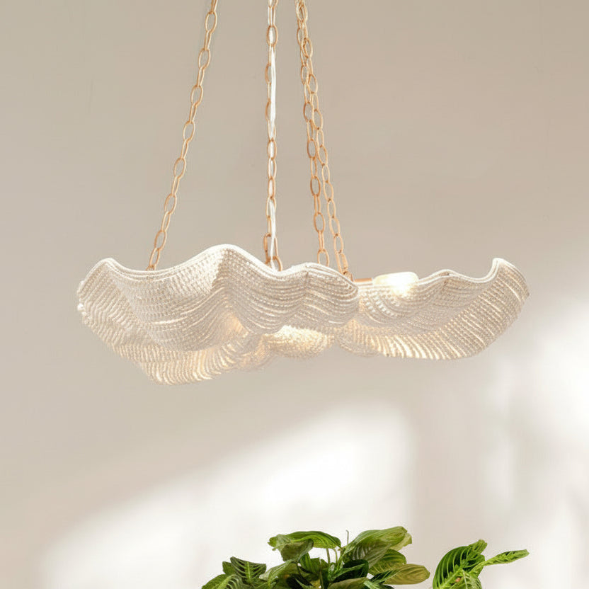 Gold shell-shaped pendant light with a plant in the foreground on a neutral background