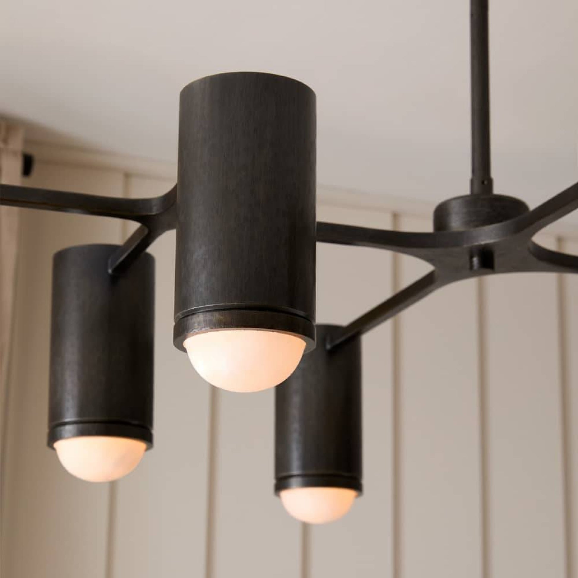 Modern black chandelier with three cylindrical lights on a neutral background