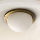 Ceiling light fixture with brass ring and white glass shade on a neutral background