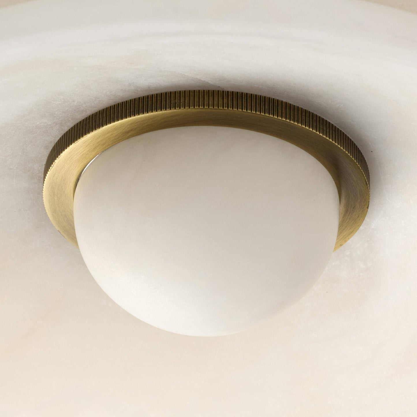 Ceiling light fixture with brass ring and white glass shade on a neutral background