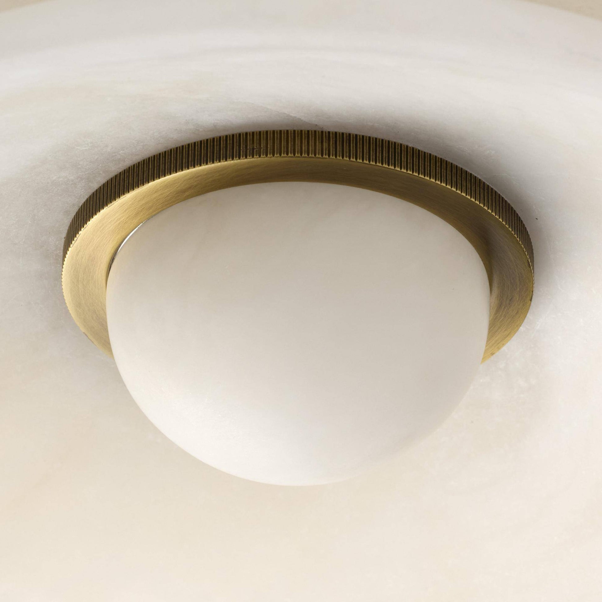 Ceiling light fixture with brass ring and white glass shade on a neutral background