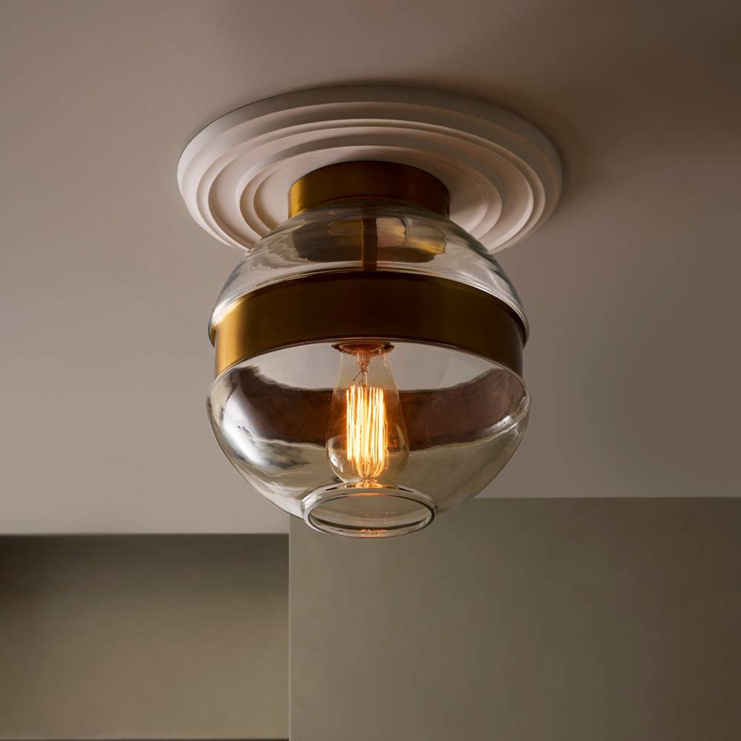 A ceiling-mounted glass globe light fixture with a warm brass band and visible Edison bulb, installed against a neutral interior wall and ceiling.