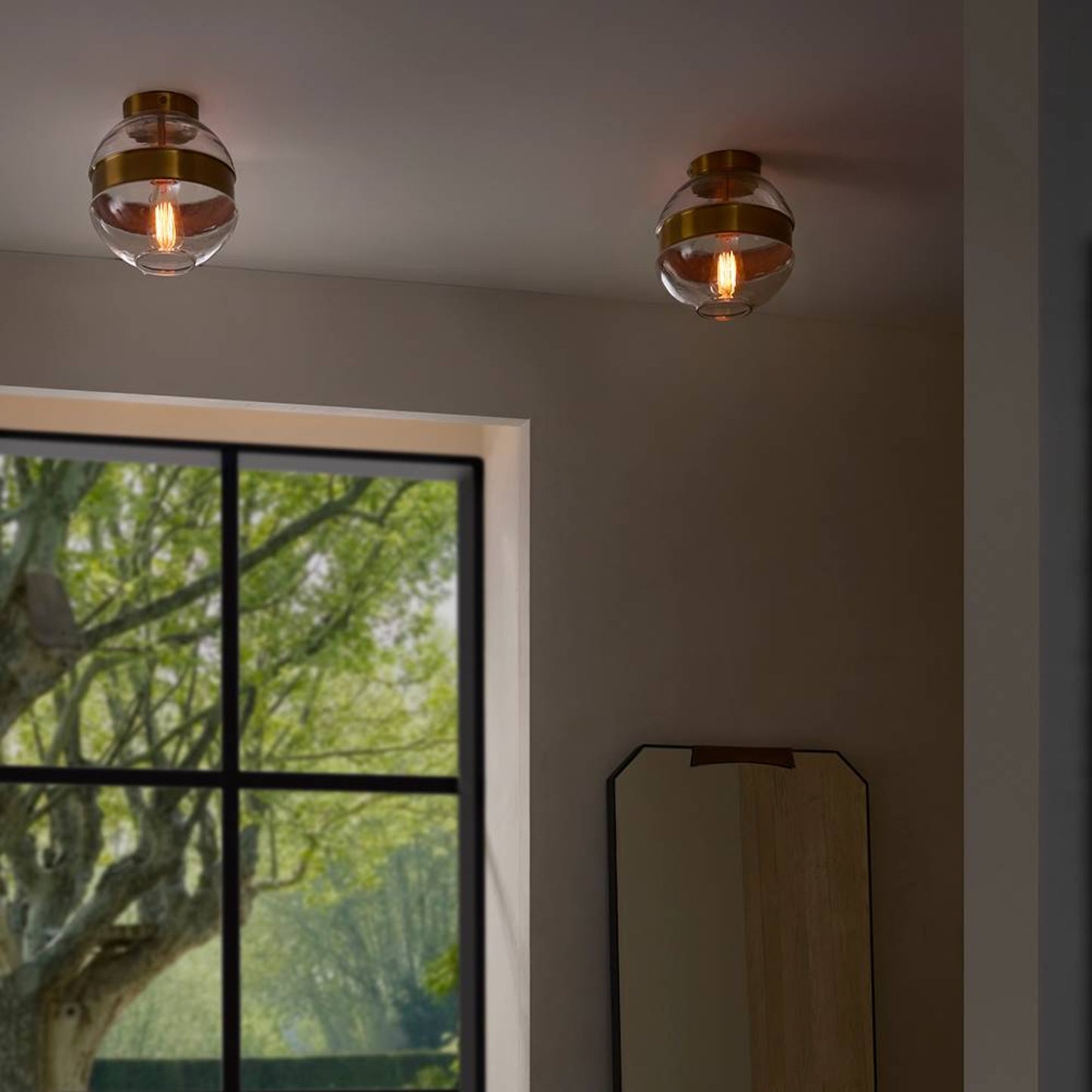 Two ceiling lights with glass shades in a room with a window showing greenery outside.