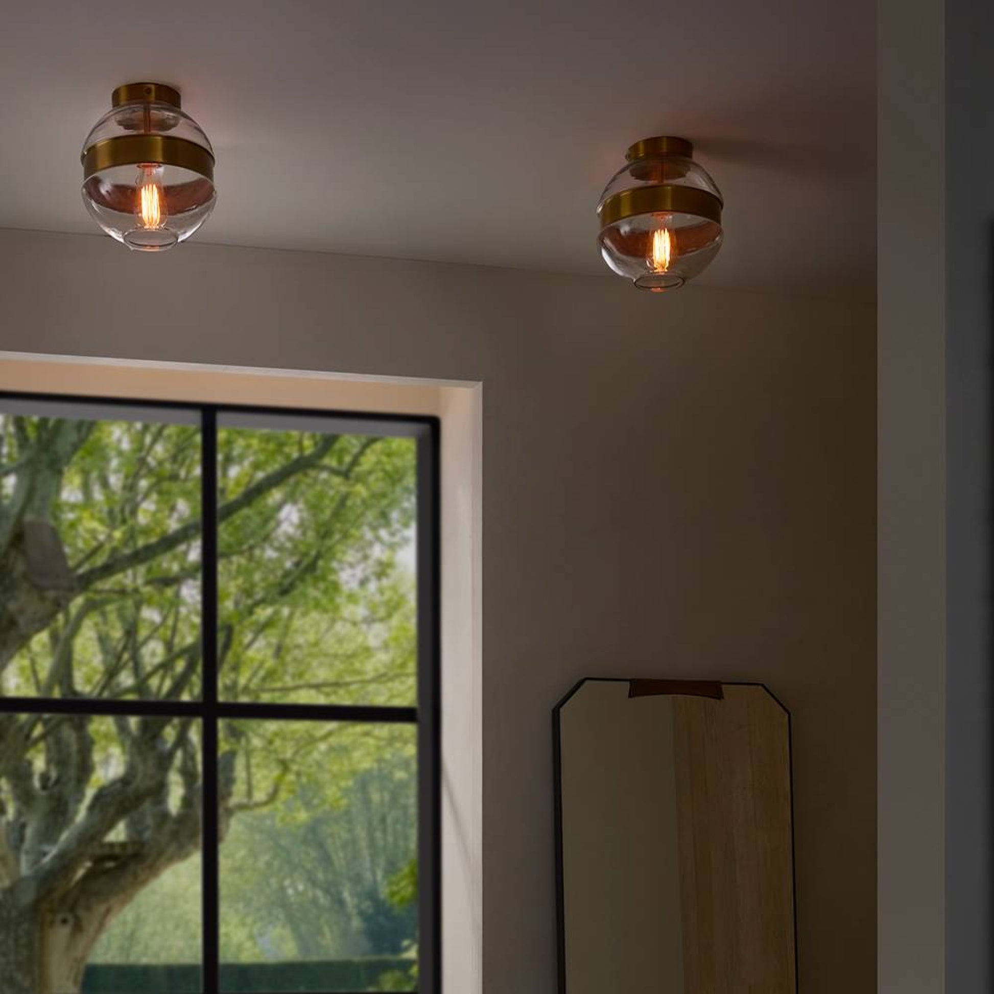 Two ceiling lights with glass shades in a room with a window showing greenery outside.