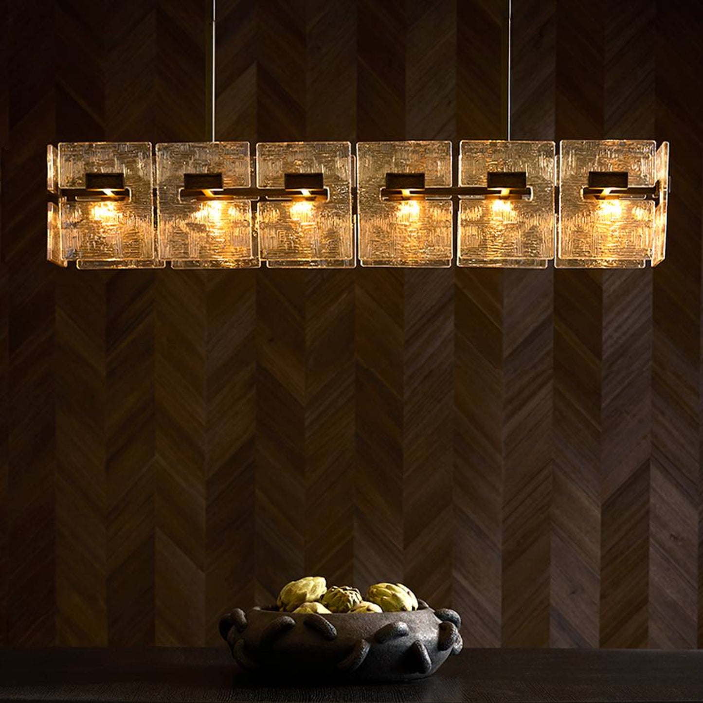 Modern chandelier with glass shades on a dark wall.