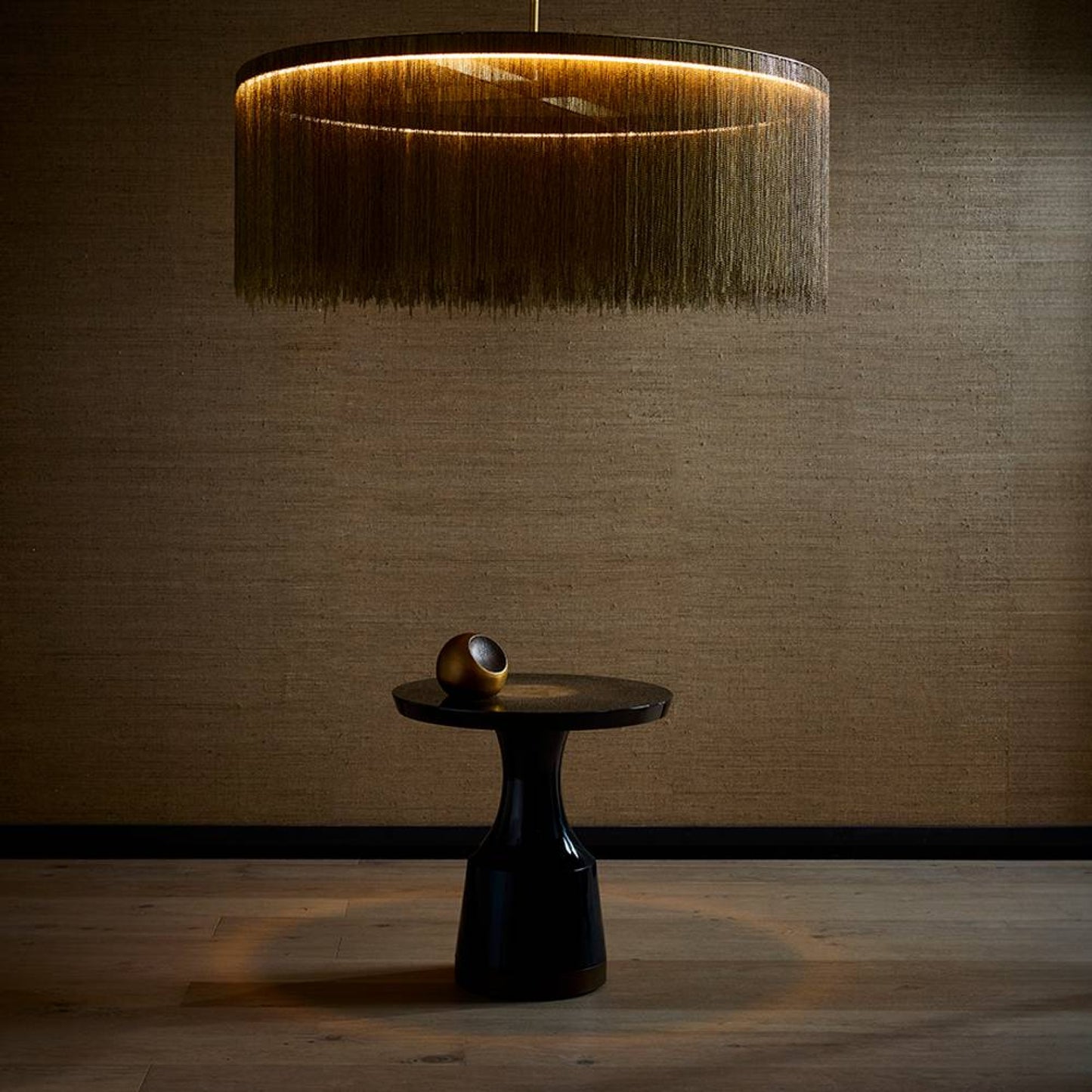 Modern pendant light with a textured shade above a black table against a textured wall.