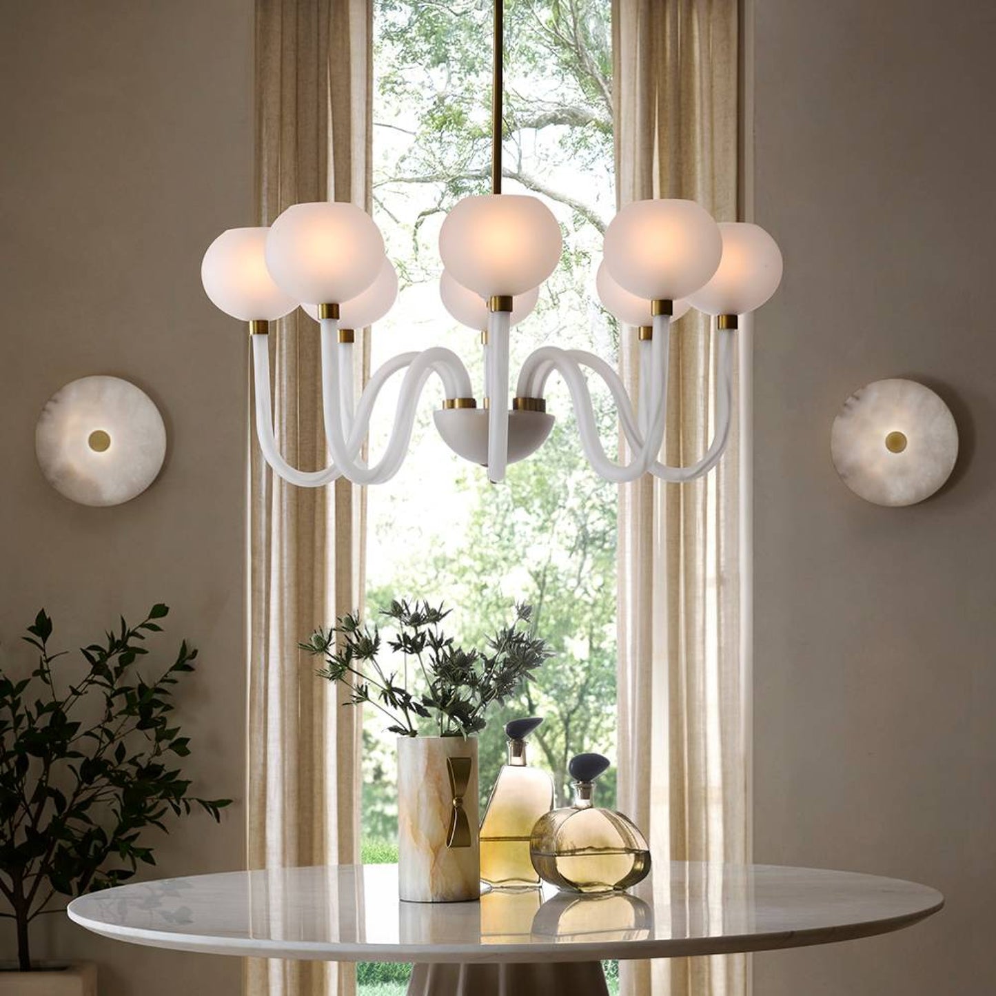 Modern chandelier hanging above a table with decor items in a room with large windows.