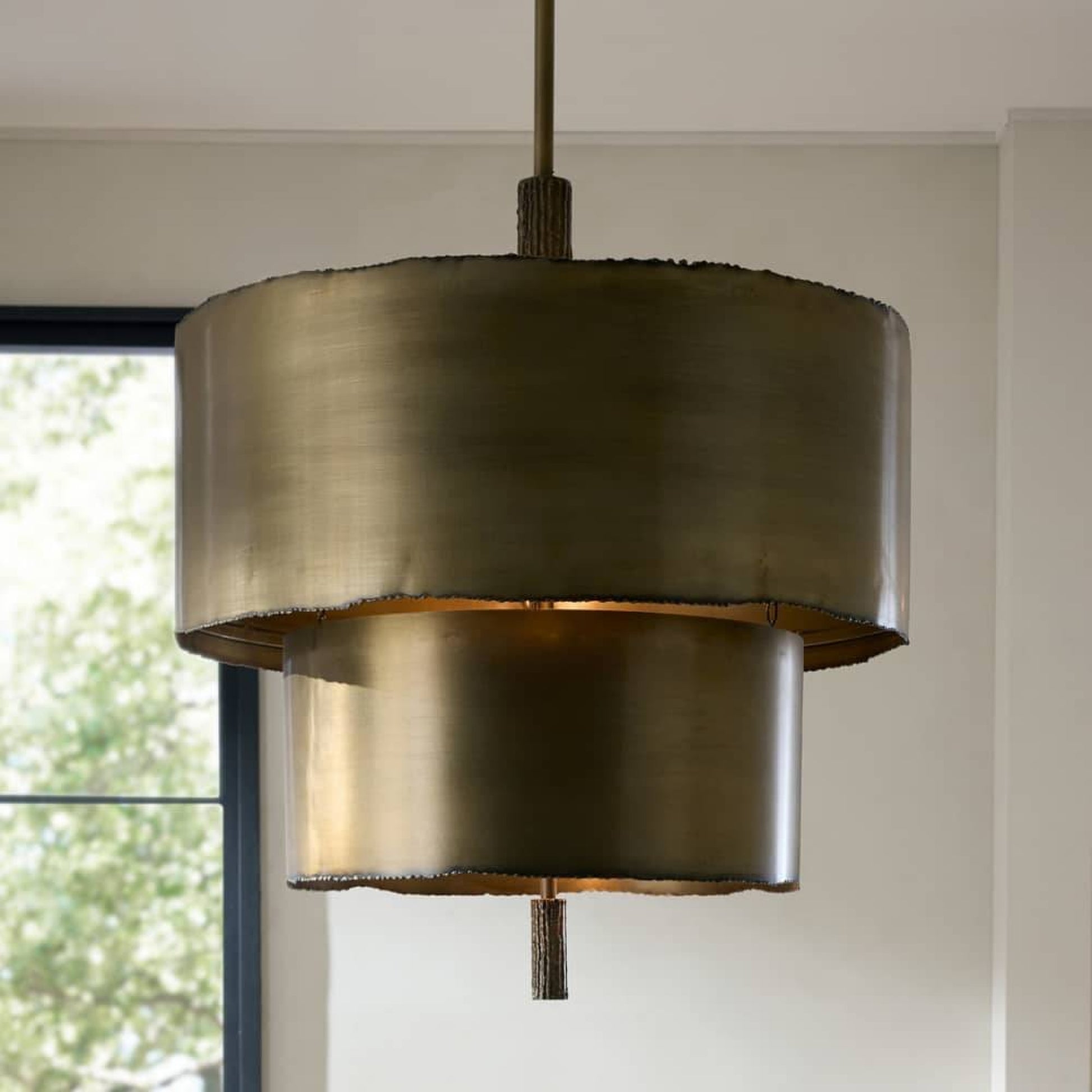 Bronze pendant light fixture hanging in a room with a window in the background