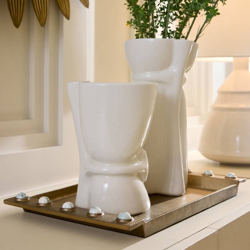 Two white ceramic vases on a decorative tray with a plant in the background