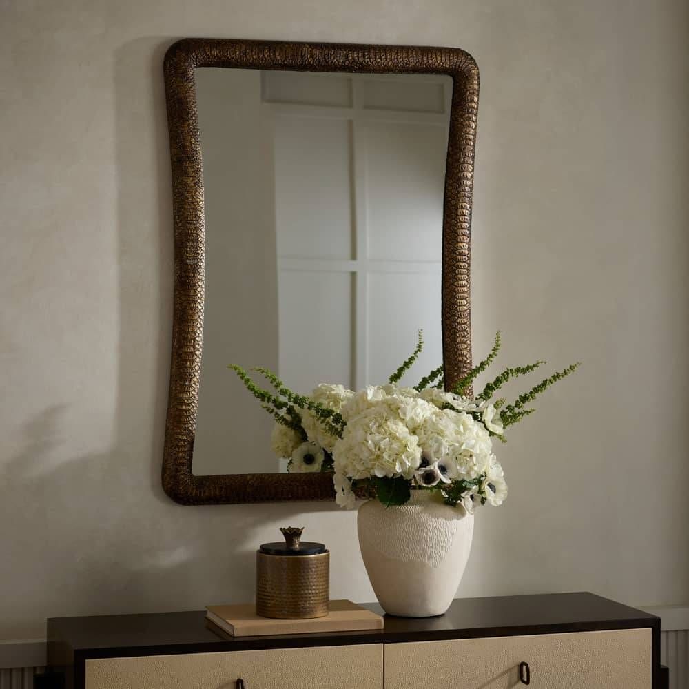 Decorative mirror with a vase of flowers on a table against a neutral wall.