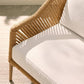 Close-up of a wicker chair with white cushion on a light wooden floor.