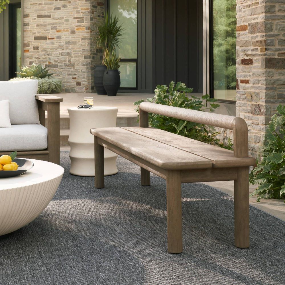 Wooden bench on a patio with outdoor furniture and plants in the background.