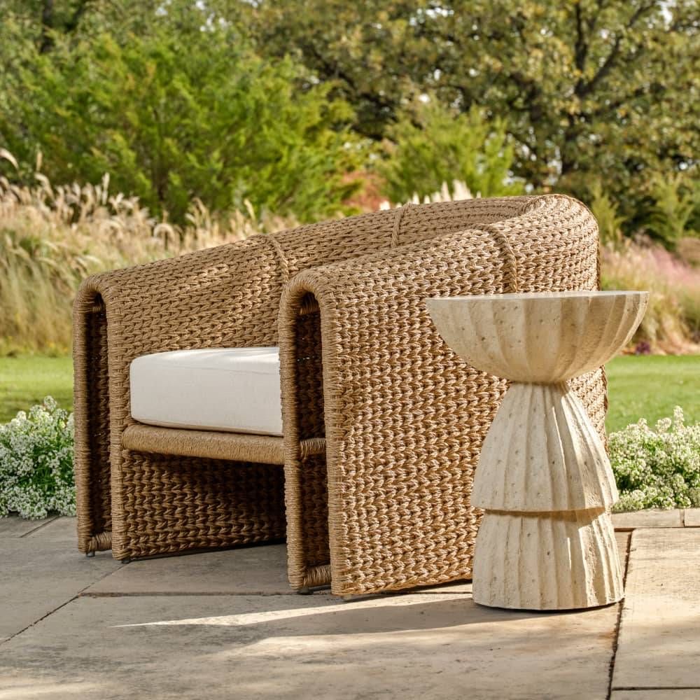 Woven outdoor chair with white cushion and matching side table on a patio