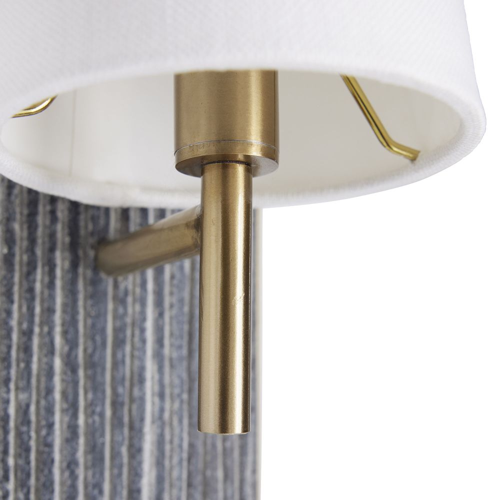 Close-up of a wall-mounted light fixture with brass arm and white shade.