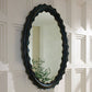 Decorative oval mirror with scalloped edge on a paneled wall