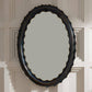 Decorative oval mirror with a black frame on a paneled wall.