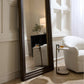 Large floor mirror in a room with a white armchair and side table.