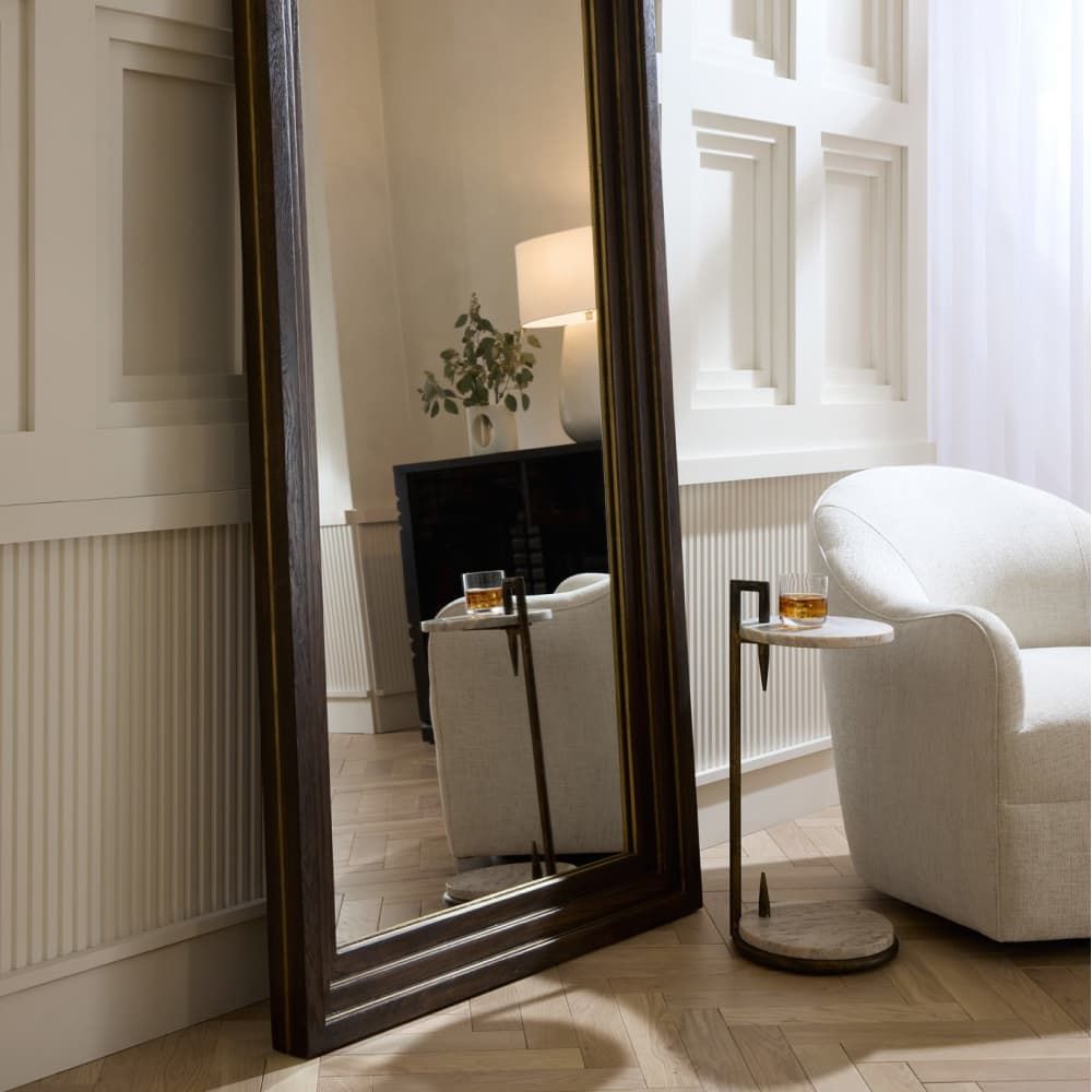Large floor mirror in a room with a white armchair and side table.