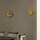 Two wall-mounted lights on a beige wall with a dining table and chairs in the foreground.