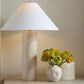 Decorative lamp with a white shade and textured base, next to a small vase with yellow flowers on a neutral background.