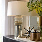 Decorative table lamp with a textured base on a console table with flowers and other decor items.