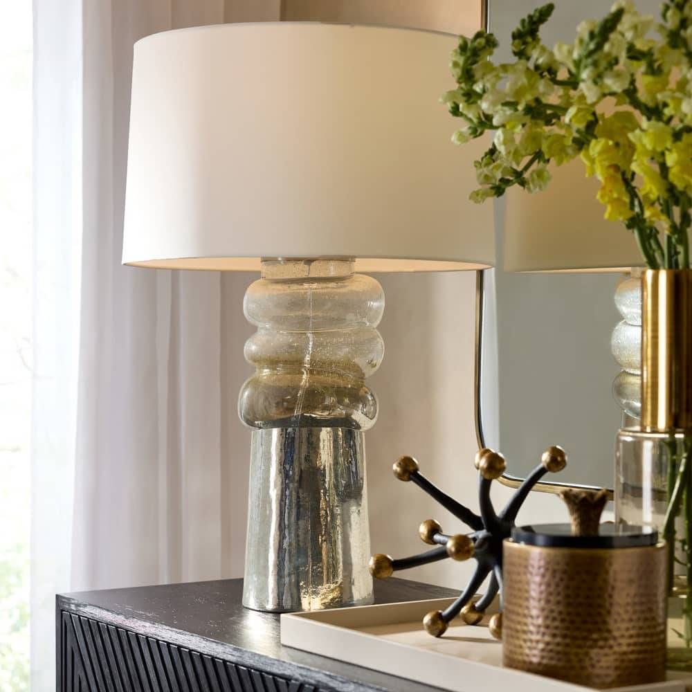 Decorative table lamp with a textured base on a console table with flowers and other decor items.