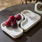 White ceramic fruit bowl with red grapes on a dark surface
