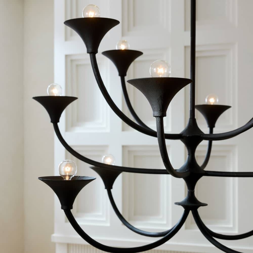 Black chandelier with multiple light bulbs against a white paneled wall.