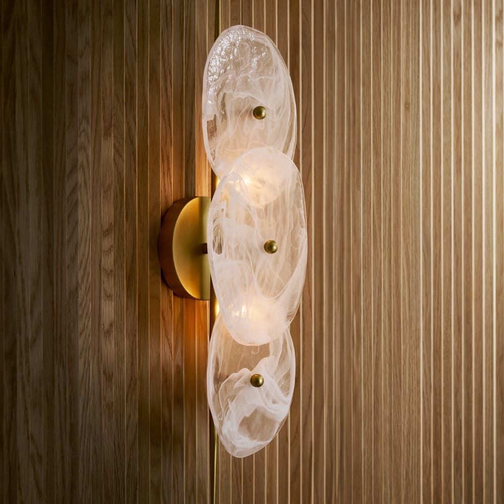 Decorative wall light fixture with glass shades on a wooden wall.