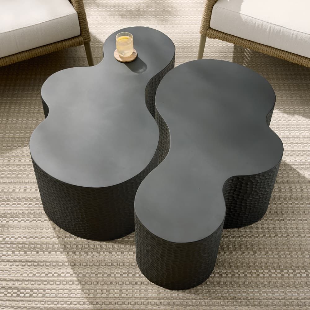 Modern black wicker coffee table with a candle on a textured floor.