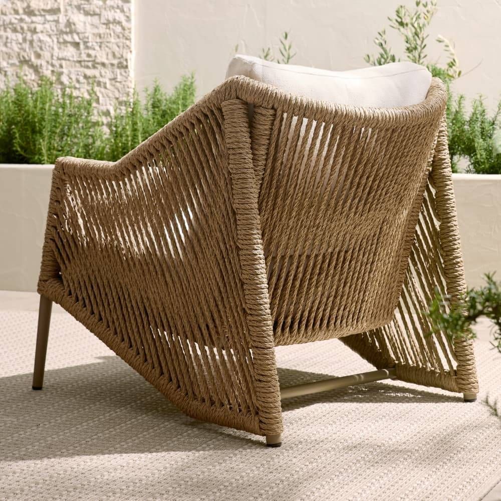 Woven chair with a white cushion on a patio with plants in the background