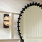 Decorative black spiral wall mirror with a light fixture on a white wall.