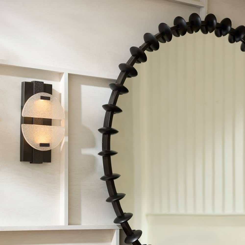 Decorative black spiral wall mirror with a light fixture on a white wall.