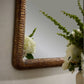 Decorative mirror with a textured gold frame on a wall with flowers in the foreground.