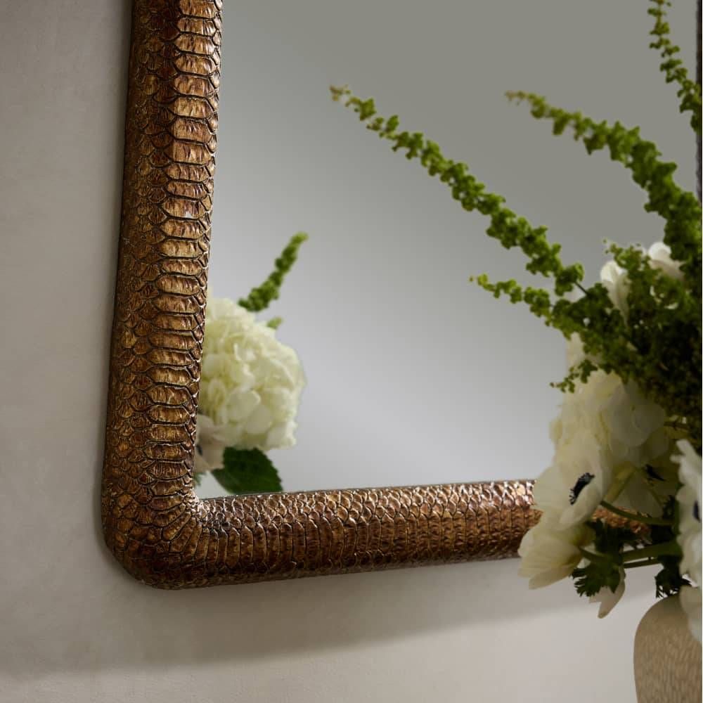 Decorative mirror with a textured gold frame on a wall with flowers in the foreground.