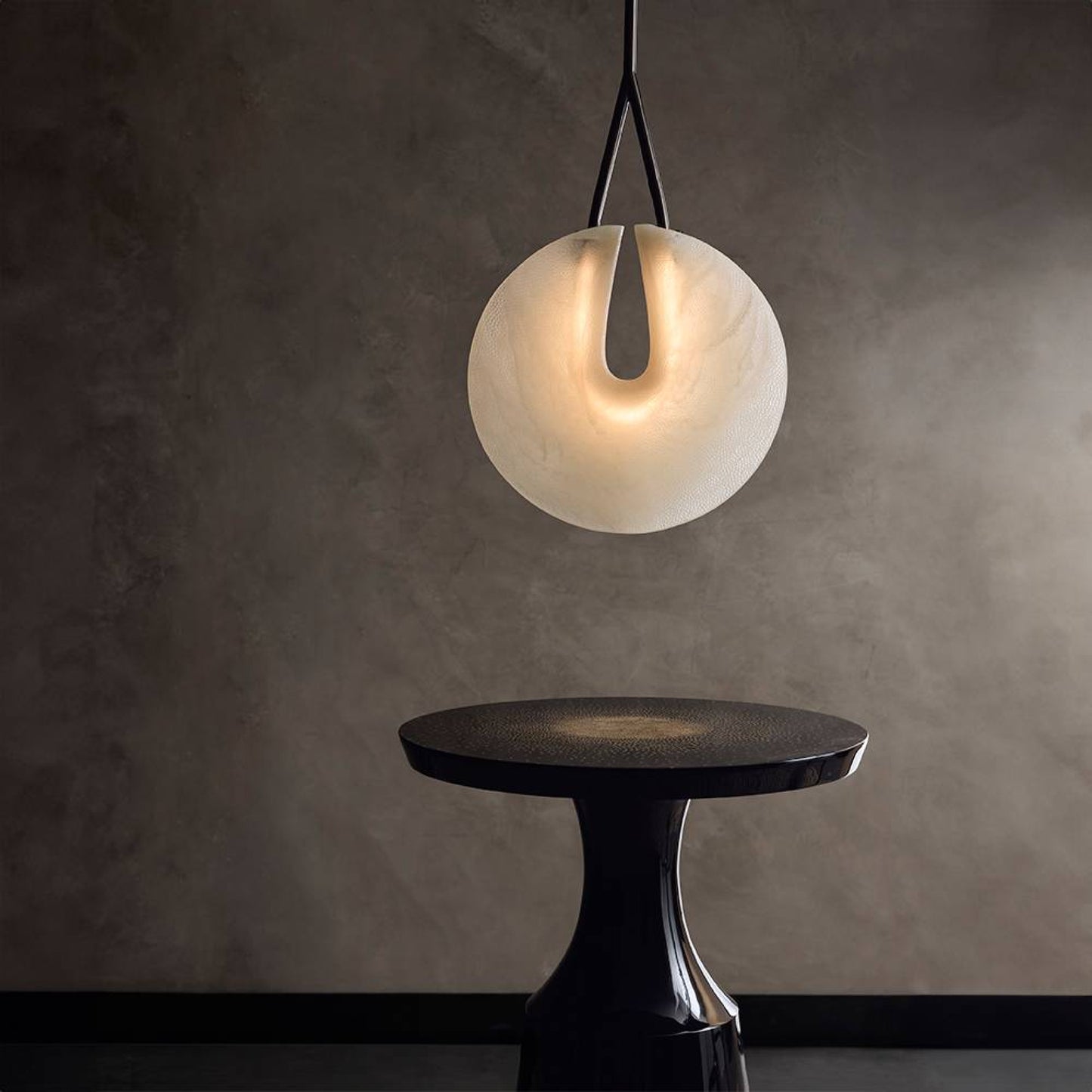 Modern pendant light hanging above a black table against a dark wall.