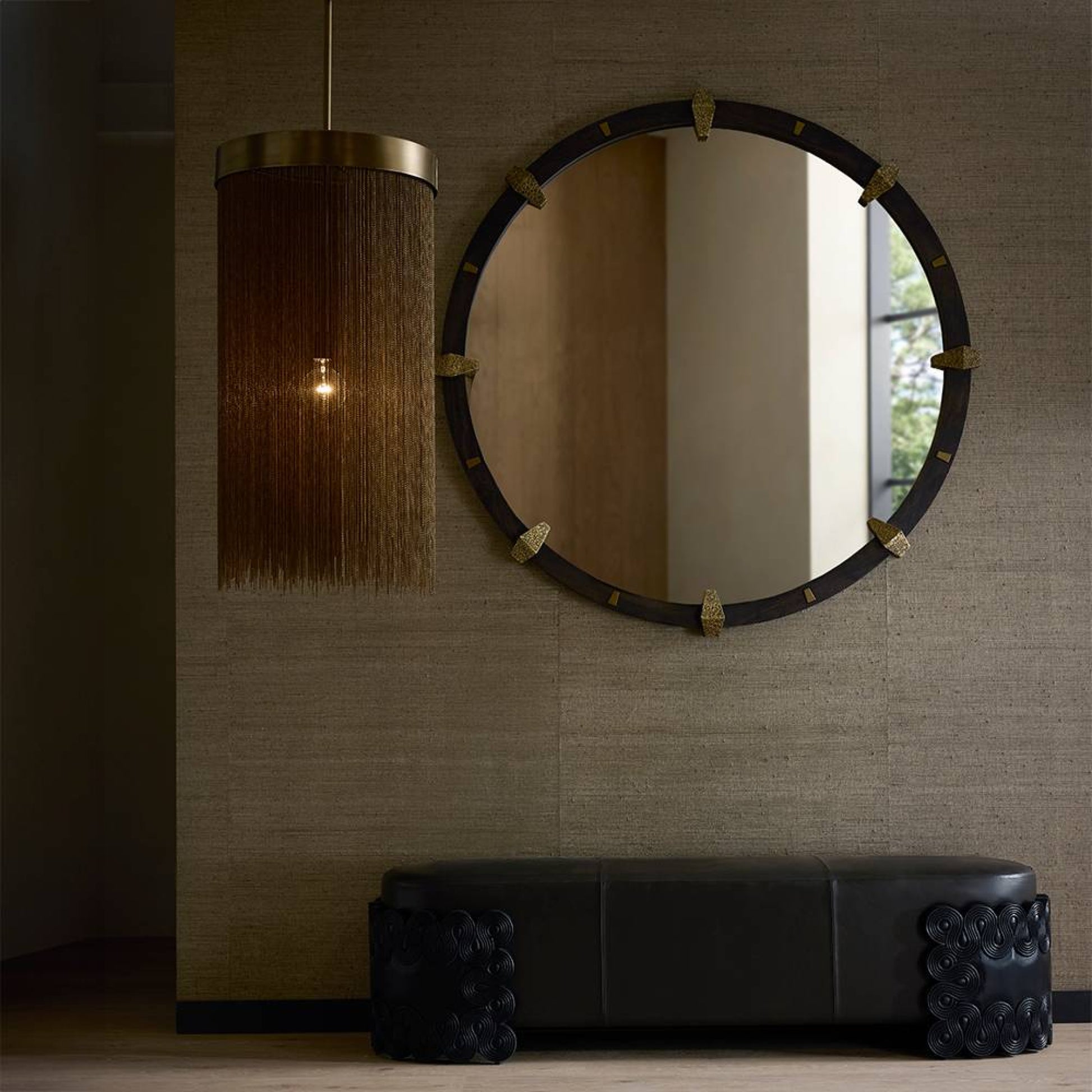 Round mirror with decorative frame on a textured wall above a black bench.