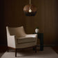 Beige armchair in a dimly lit room with a woven pendant light and small table.