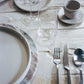 Dining table setting with plates, glasses, cutlery, and a napkin on a textured surface.