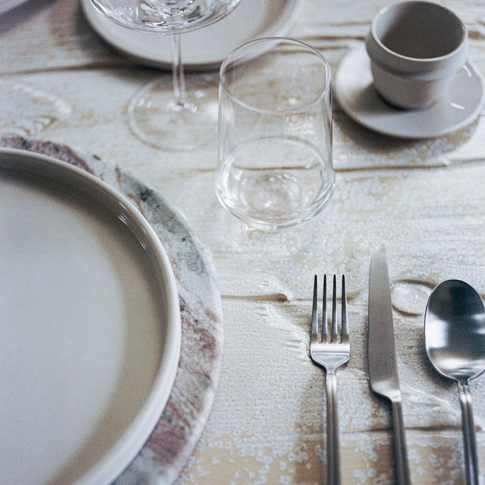 Dining table setting with plates, glasses, cutlery, and a napkin on a textured surface.
