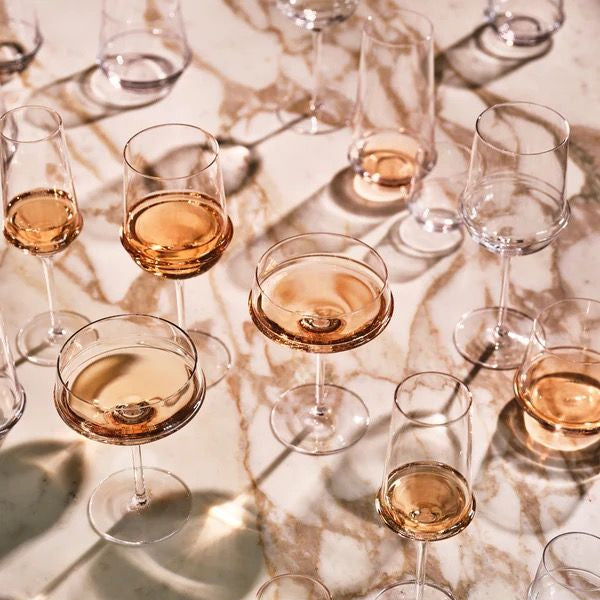 Multiple glasses of rose gold liquid arranged on a reflective surface