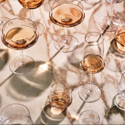 Multiple wine glasses filled with a amber-colored liquid on a marble surface.