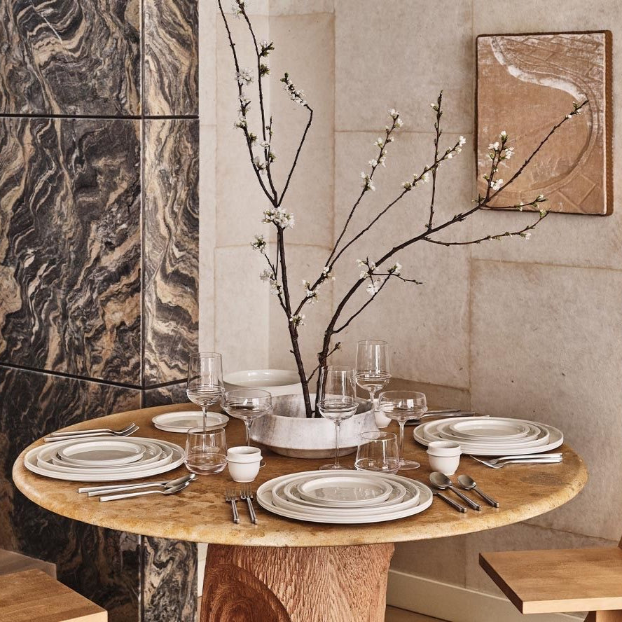 Dining table set with plates, glasses, and a decorative branch in a modern kitchen.